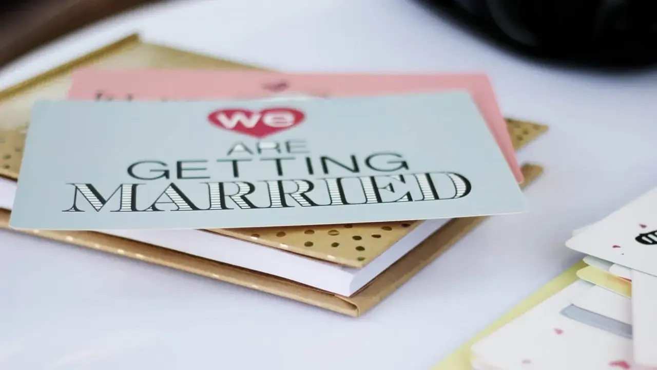Zaproszenia ślubne "We are getting married" w formacie B0, ułożone na złotym notesie.