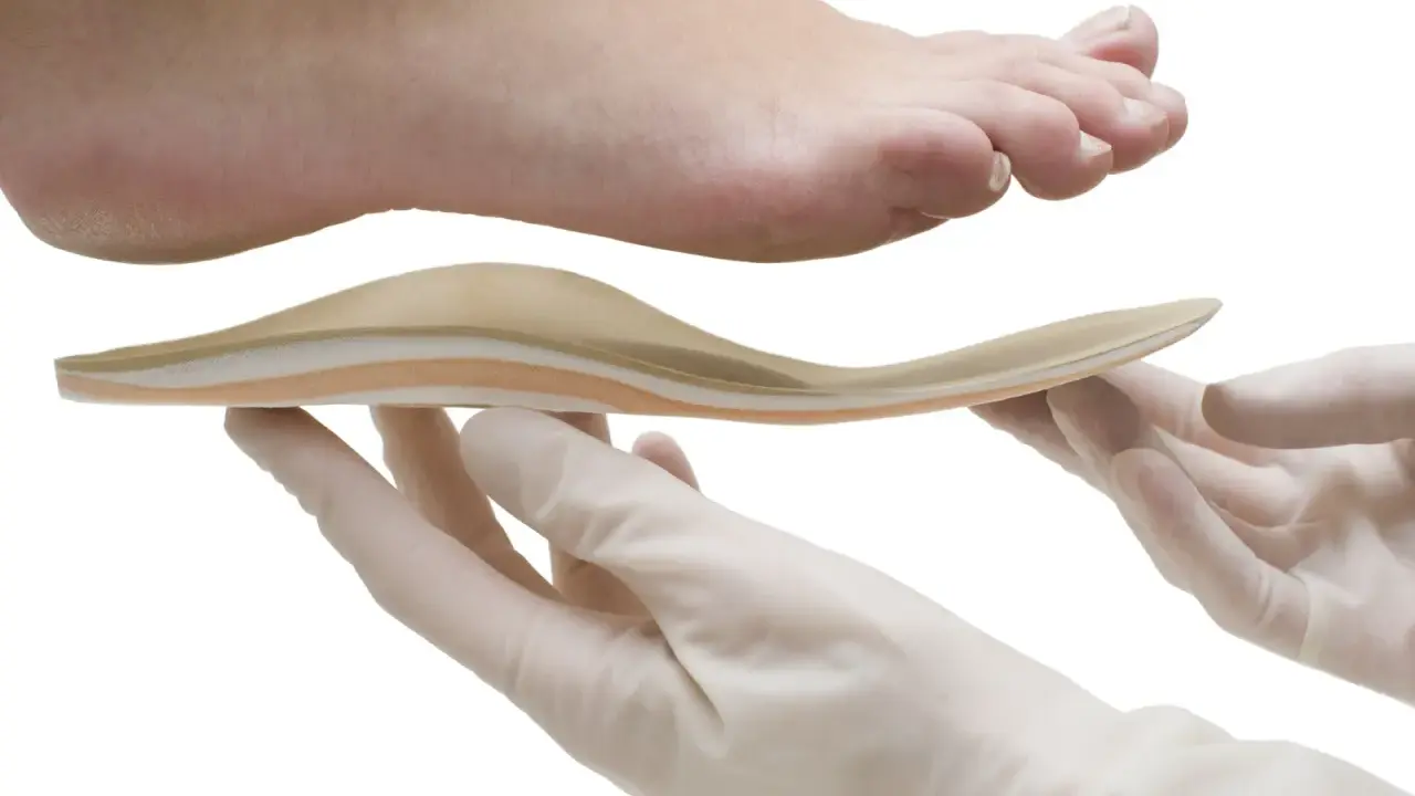 Une orthoplastie sur mesure est présentée sous un pied, tenue par des mains gantées.