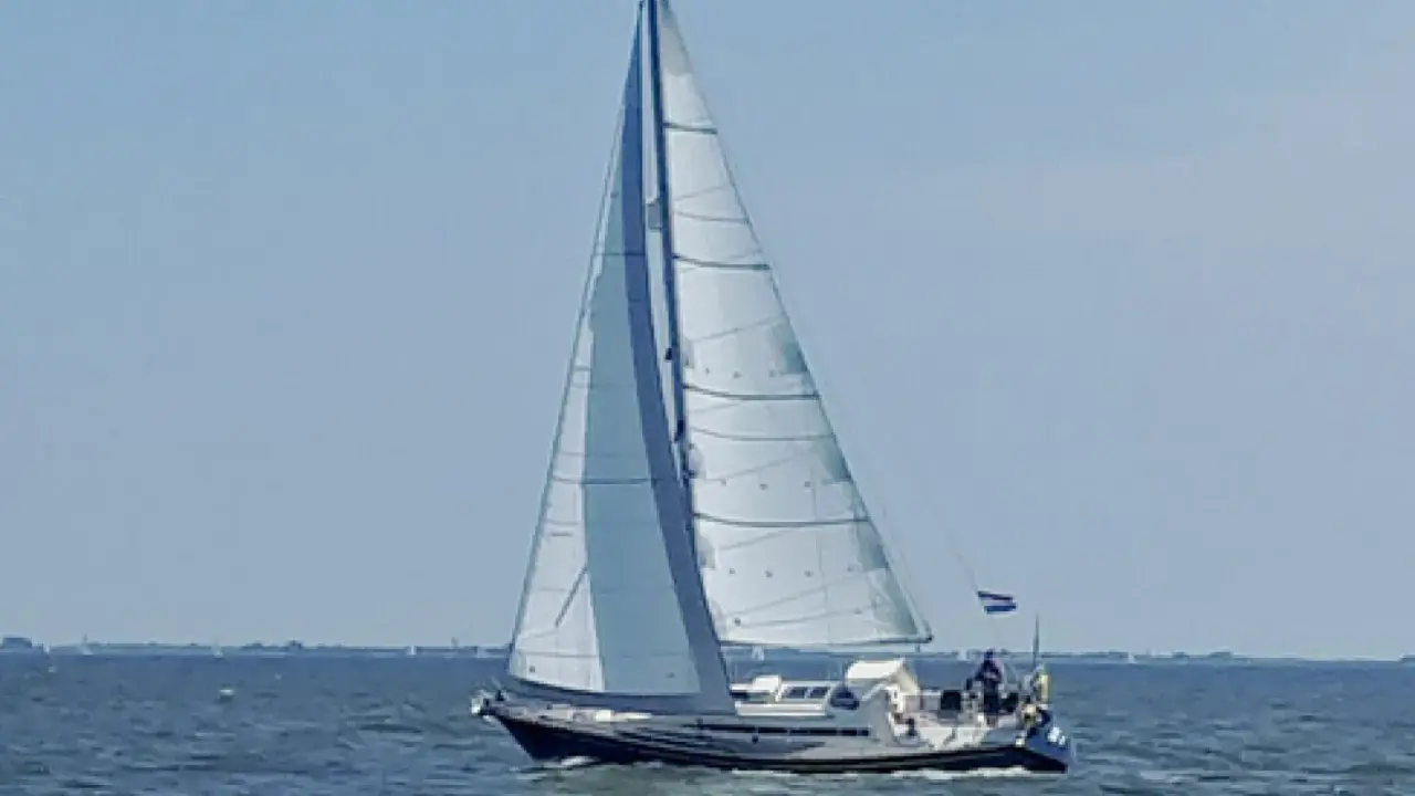 Voilier blanc et bleu naviguant sur une mer calme sous un ciel clair. Les voiles sont gonflées par le vent. Les premiers 375 avis sur ce type de bateau sont positifs.