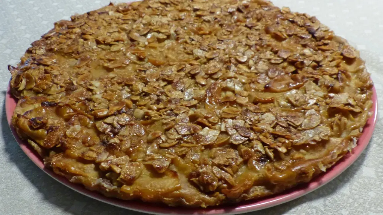 Gâteau rustique aux pommes et amandes effilées sur une assiette rose.