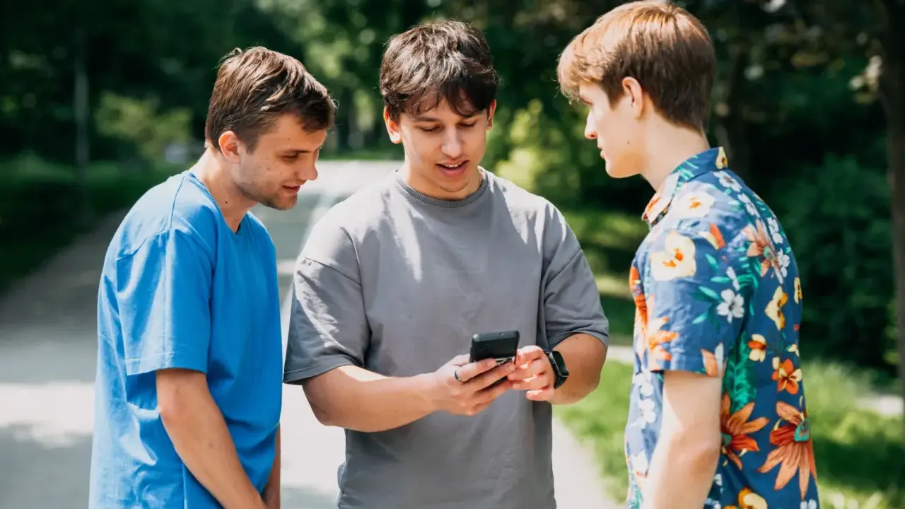 Trzech studentów dyskutuje, czy na studiach są wakacje. Jeden z nich pokazuje coś na telefonie.
