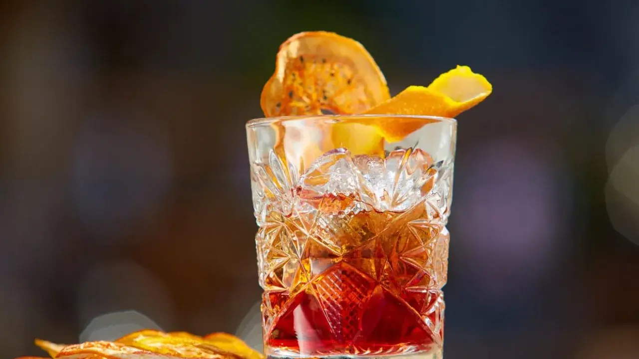 Klasyczny whisky old fashioned w kryształowej szklance, ozdobiony skórką pomarańczy i suszonym owocem.