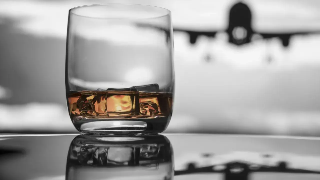 Szklanka whisky z lodem na tle samolotu w locie.