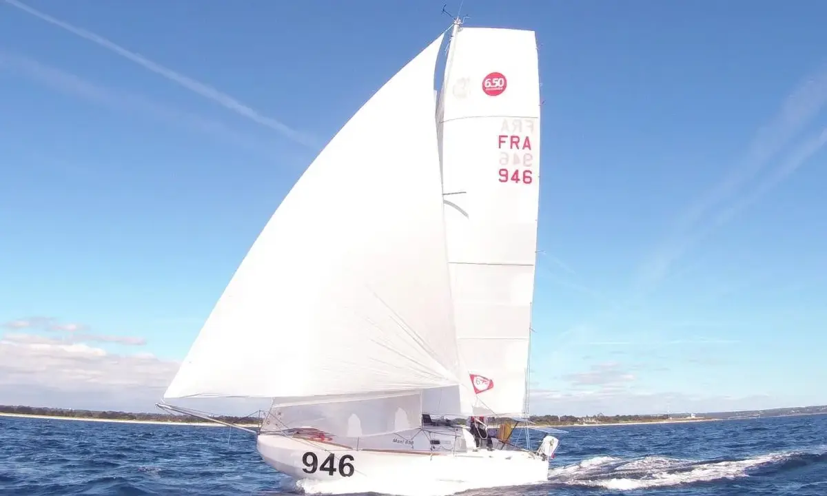 Un voilier de la classe mini, numéro 946, navigue sur une mer bleue sous un ciel clair.