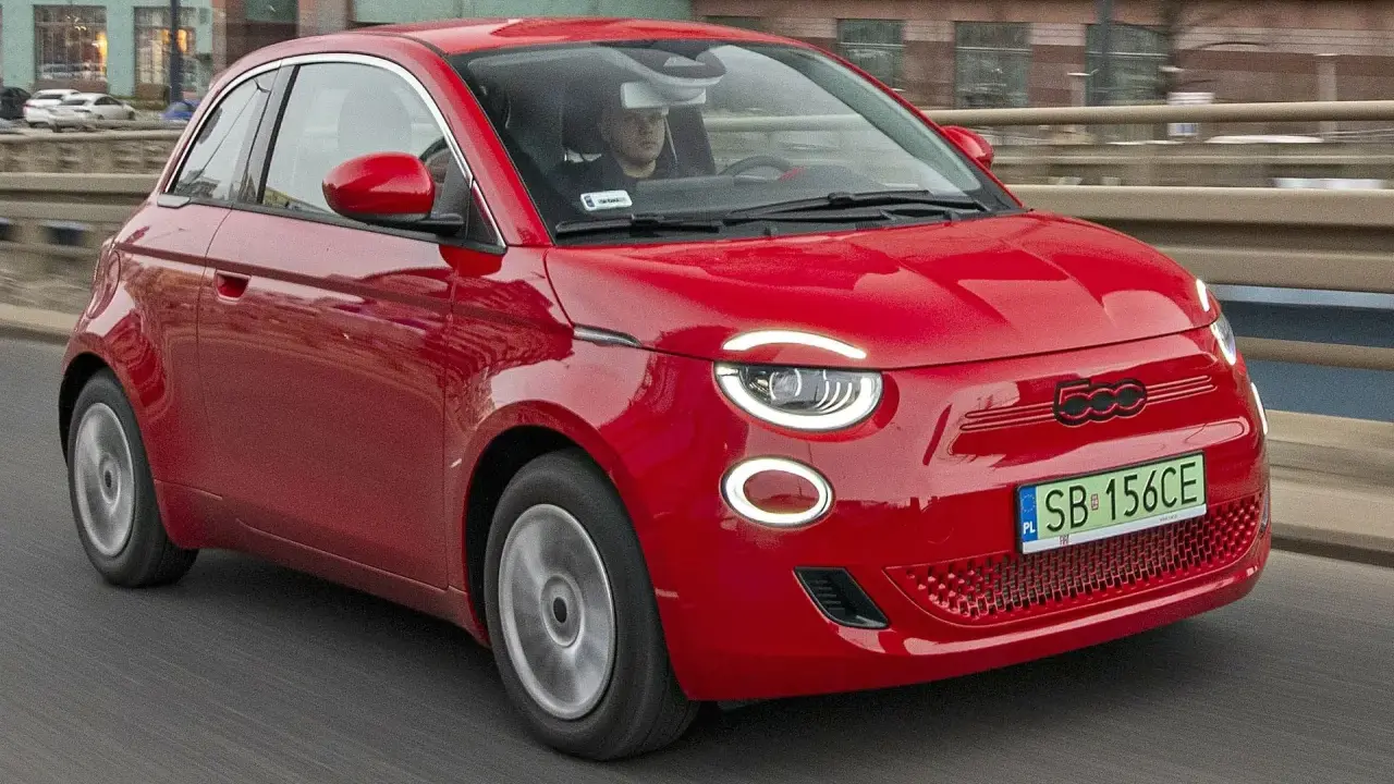 Czerwony Fiat 500 jedzie po drodze. Sprawdź aktualną fiat 500 cena i dowiedz się więcej o tym stylowym samochodzie.