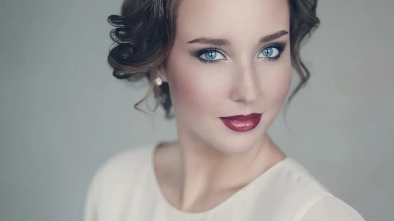 Maquillaje para vestido blanco: ojos ahumados y labios rojos intensos, peinado recogido con rizos.