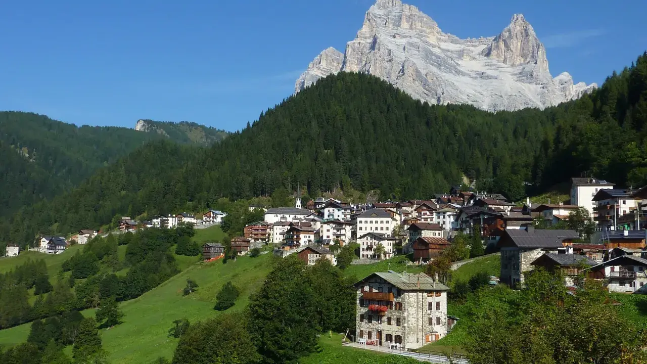 Villaggio alpino con case in pietra e legno, circondato da boschi e verdi pascoli, sotto un'imponente cima rocciosa. Il rifugio Venezia è un luogo incantevole.