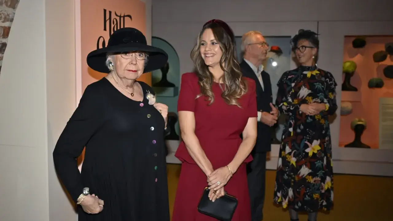Prinsessan Sofia beundrar en utställning med hattar, där en äldre dam bär en elegant svart hatt.