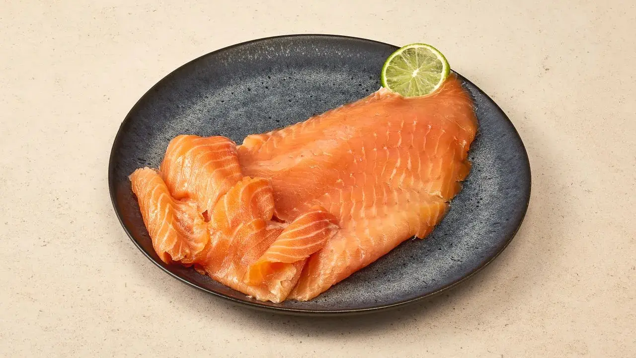 Räucherlachs auf dunkler Platte, garniert mit einer Limettenscheibe. Perfekt für einen Caipirinha-Lachs-Genuss.