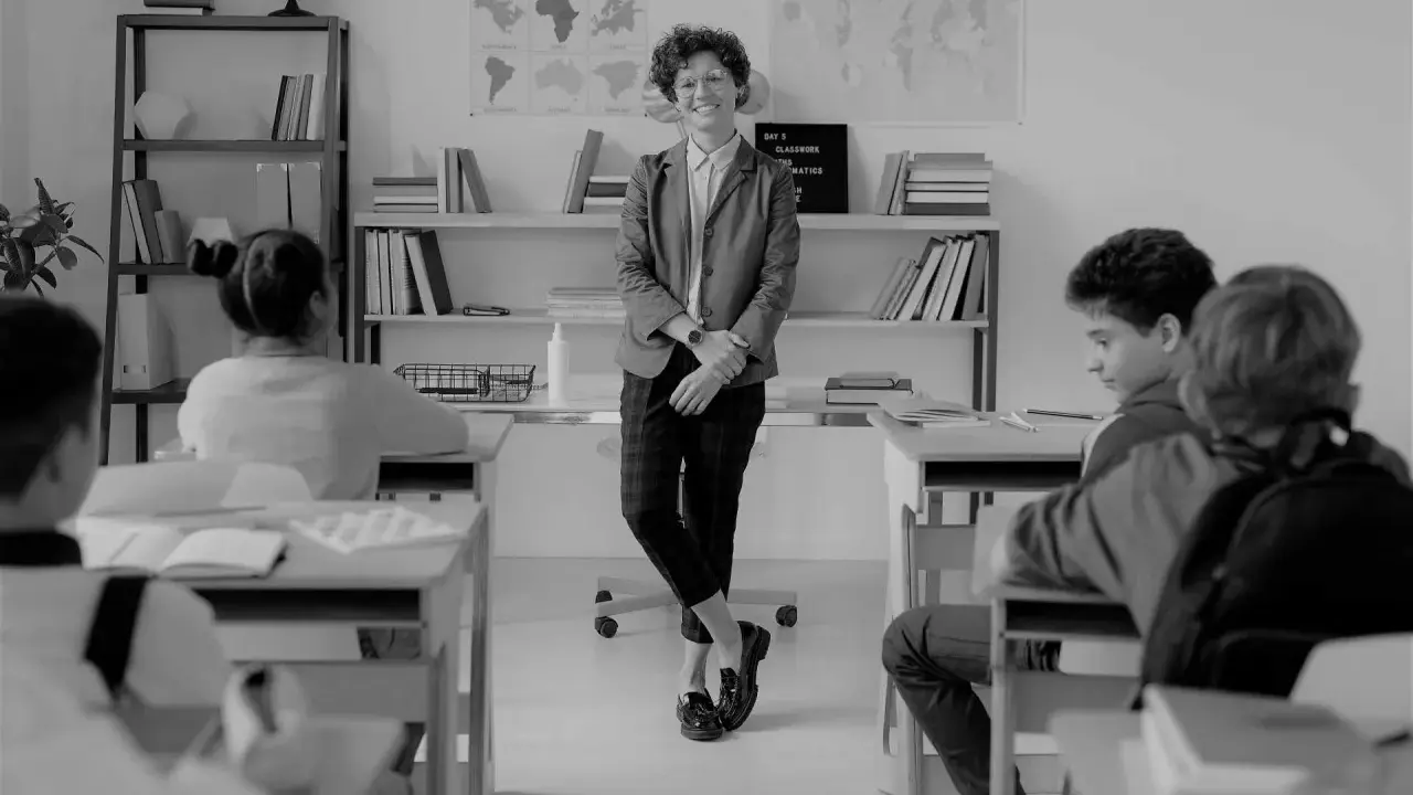 Lehrerin lächelt in einem Klassenzimmer, während Schüler an ihren Tischen sitzen. Eine Szene, die eine gute Klassengemeinschaft widerspiegelt.