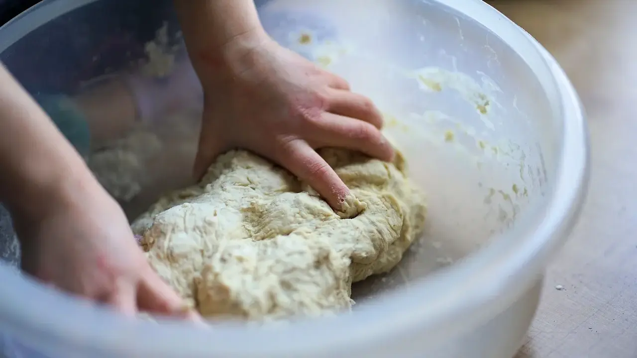 Mains d'enfant pétrissant une pâte à pizza dans un bol. Une étape clé de la recette pâte à pizza levure sèche.