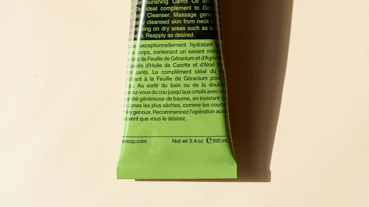 Tubo verde brillante di Aesop con testo in inglese e francese. Il testo descrive un balsamo corpo idratante, spiegando il suo inci significato e gli ingredienti chiave.