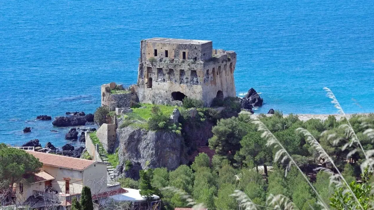 Torre aragonese a picco sul mare, uno dei borghi da visitare in Calabria, con case e vegetazione lussureggiante.