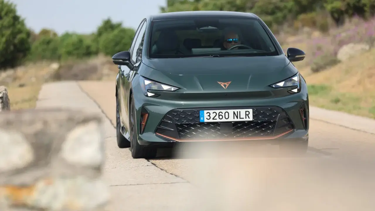 La Cupra Born VZ, d'un vert profond, roule sur une route de campagne. Un conducteur porte des lunettes de soleil.