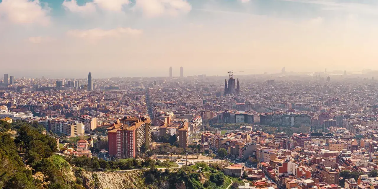 Panorama von Barcelona von oben. Die Sagrada Familia und moderne Wolkenkratzer ragen aus der weitläufigen Stadt hervor.