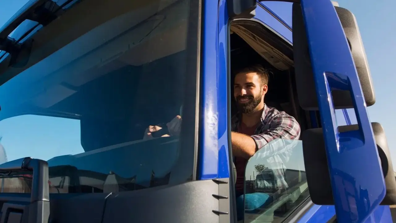 Un camionista sorridente al volante, pronto per un nuovo viaggio. Il suo stipendio camionista è meritato per il duro lavoro su strada.