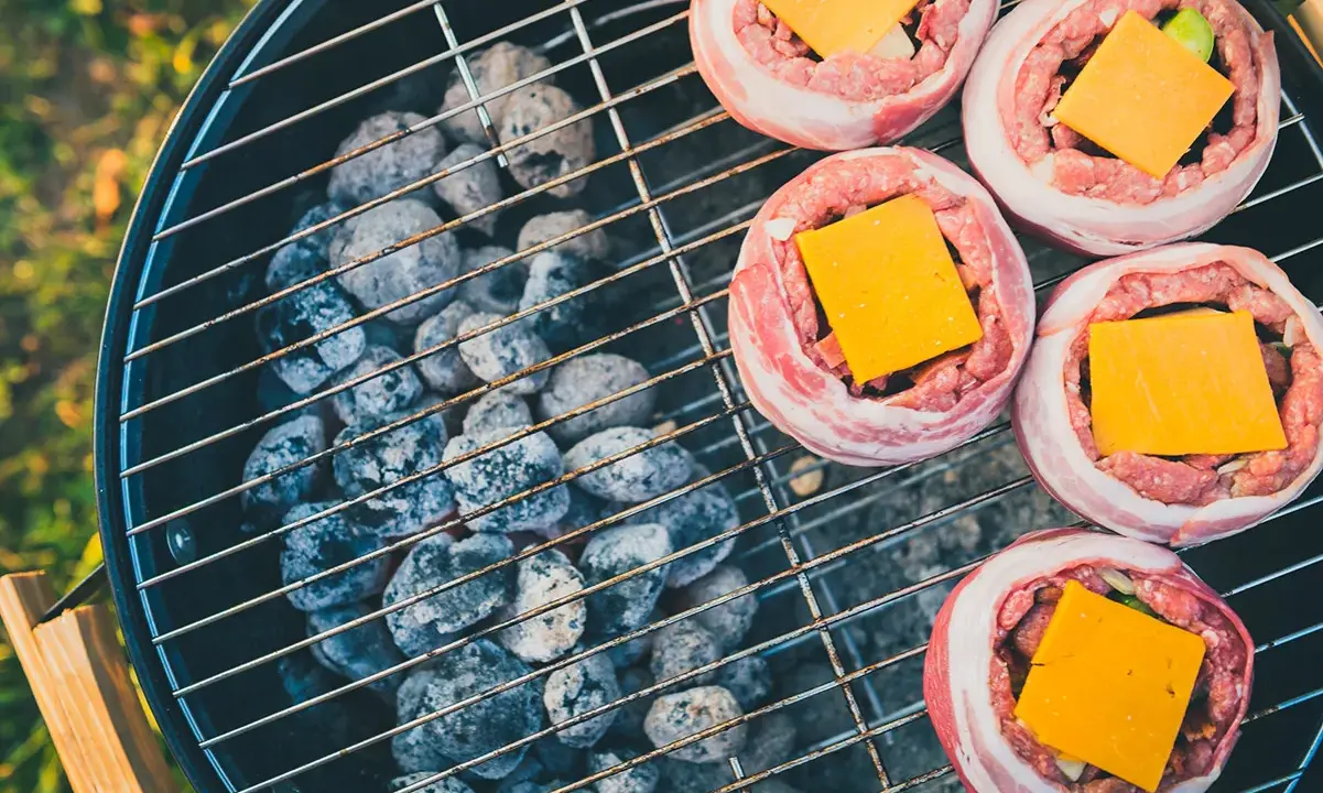 Fem baconsnurrade köttfärsbiffar med ost på en grill för indirekt grillning.