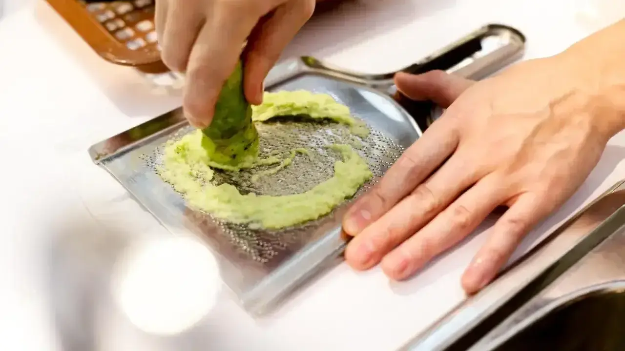 Ręka trze korzeń wasabi o tarkę. To właśnie tak powstaje świeże wasabi, które dodaje ostrości potrawom.