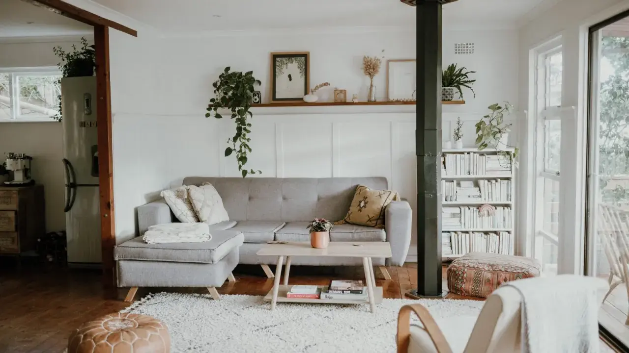 Przytulny salon w stylu skandynawskim nowoczesnym. Szara kanapa, drewniany stolik, regał z książkami i mnóstwo zieleni tworzą relaksującą atmosferę.