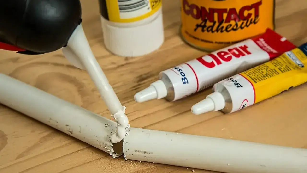 Klej w pistolecie aplikowany na pękniętą białą rurkę. Obok tubki z klejem "Clear" i puszka "Contact Adhesive" - idealne, by dowiedzieć się, czym skleić plastik.