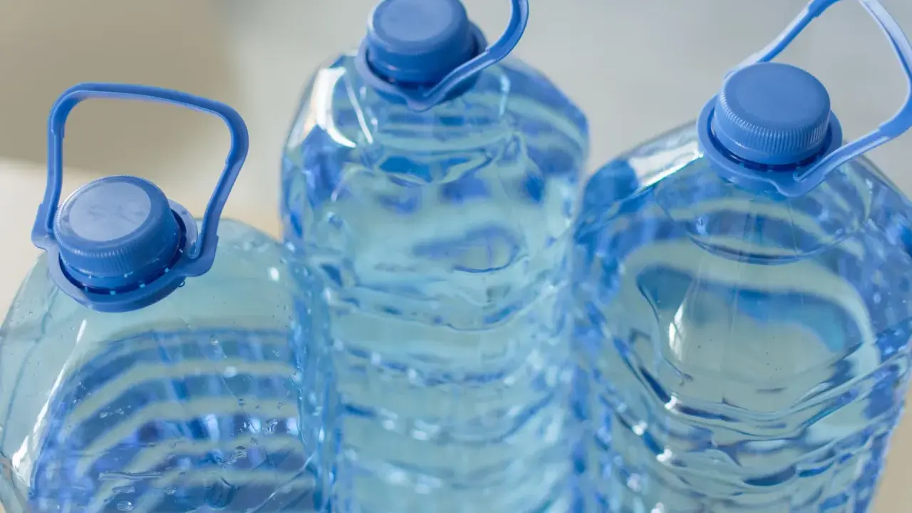 Trzy duże, niebieskie butelki z wodą, każda z uchwytem. Zastanawiasz się, ile może stać woda w plastikowej butelce po otwarciu?