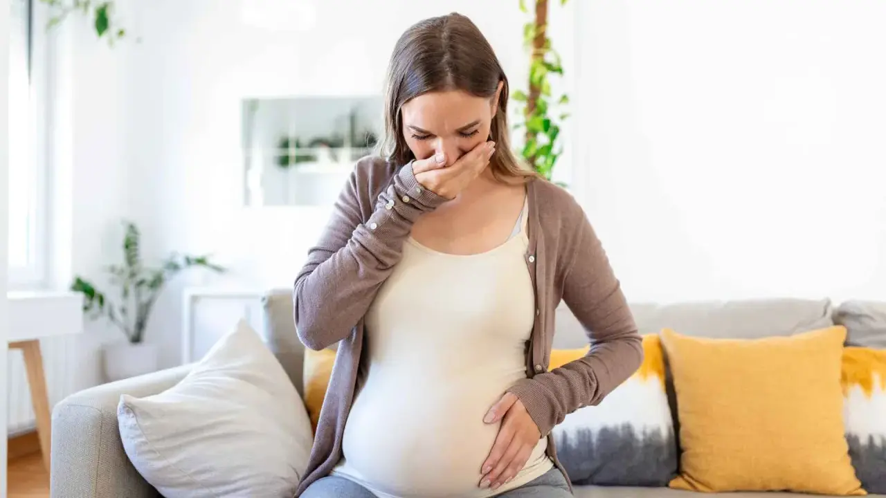 Donna incinta con nausea nel terzo trimestre, copre la bocca con la mano.