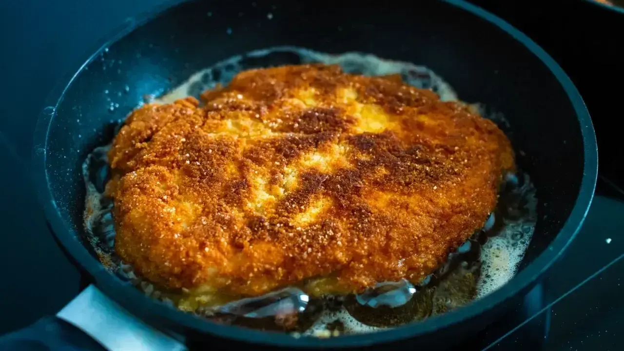 Złocisty kotlet schabowy smaży się na patelni. Idealnie chrupiąca panierka i bulgoczący tłuszcz świadczą o tym, jak długo smażyć schabowe, by były perfekcyjne.