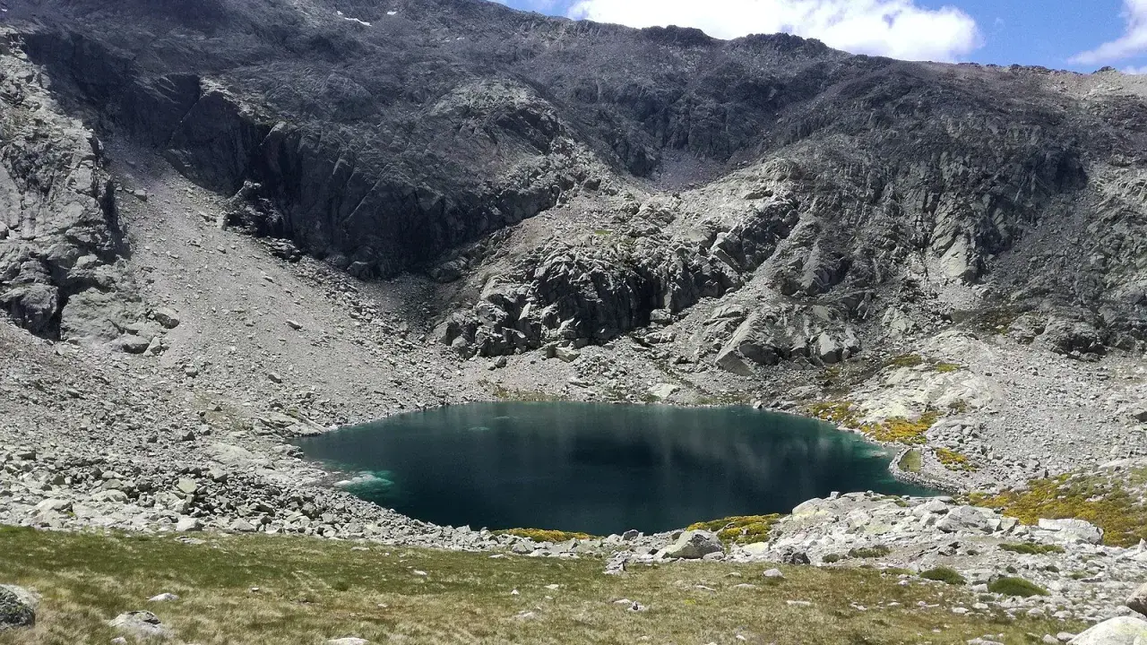 Ein tiefblauer Bergsee in der Sierra de Gredos, umgeben von felsigen Hängen und grünen Wiesen.