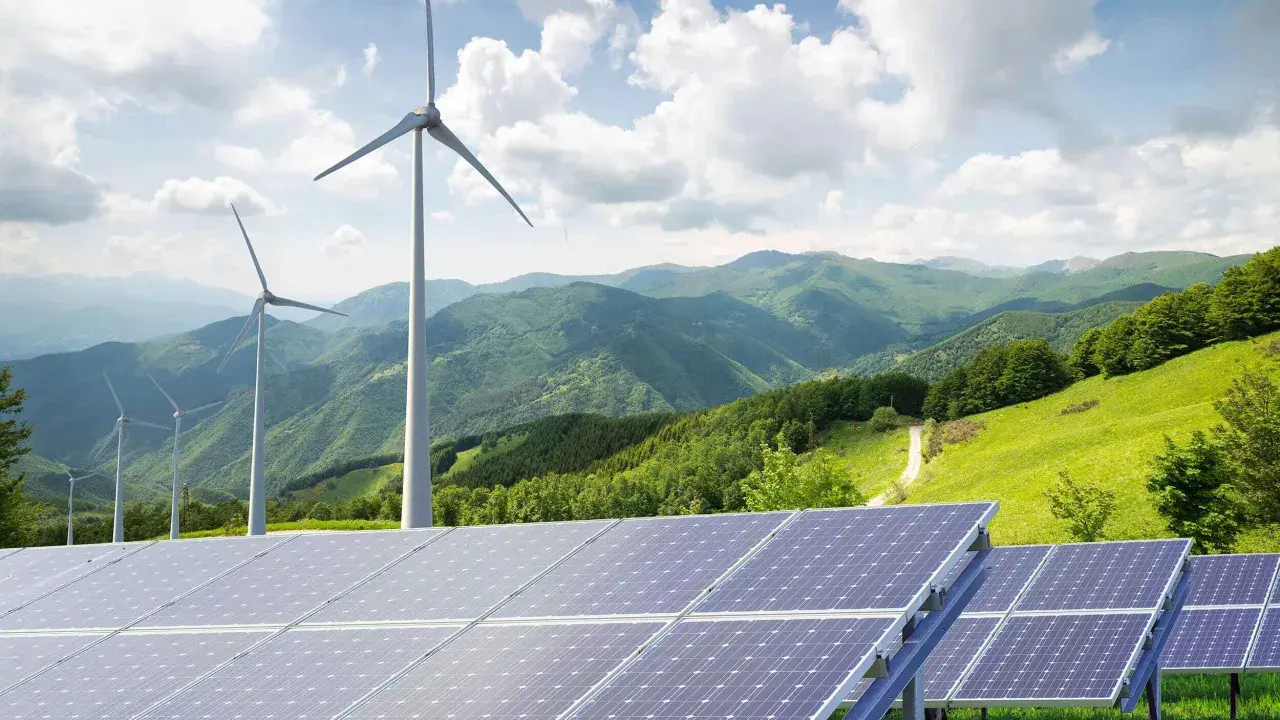 Paneles solares y aerogeneradores en un paisaje montañoso verde. La energía renovable, como la solar y la eólica, complementa la idea de un futuro sostenible, similar a cómo un generador de biomasa podría integrarse.