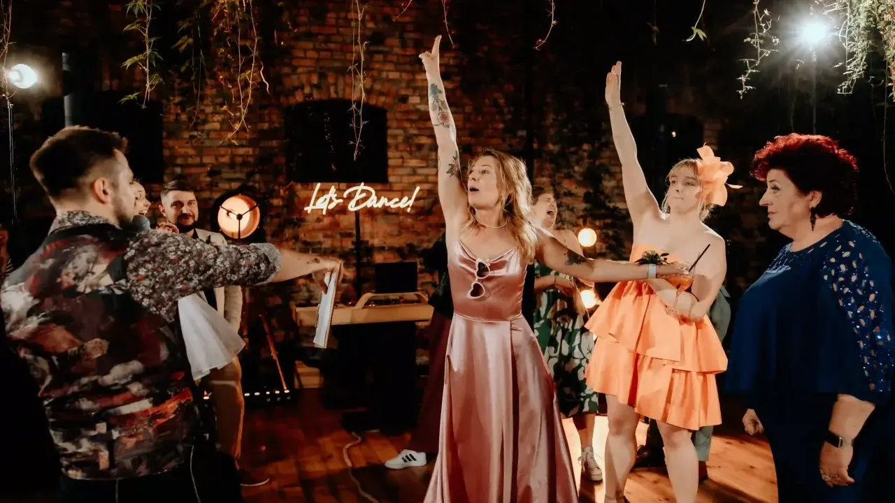 Nowoczesne oczepiny w blasku neonu "Let's Dance!". Kobiety w sukniach unoszą ręce, celebrując radosny moment.