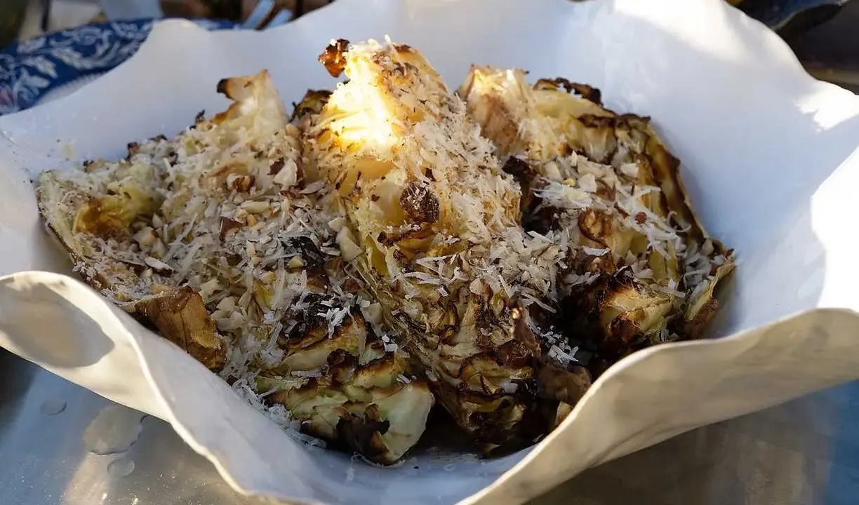 Grillad spetskål serverad i en vit skål, toppad med riven ost och hackade nötter. En härlig rätt för grillkvällen.
