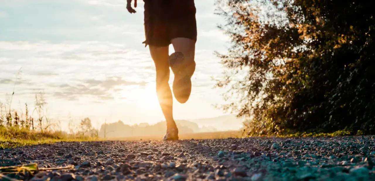Gambe di un corridore su un sentiero sterrato al tramonto. Ottimo per bruciare calorie corsa 7 km/h.