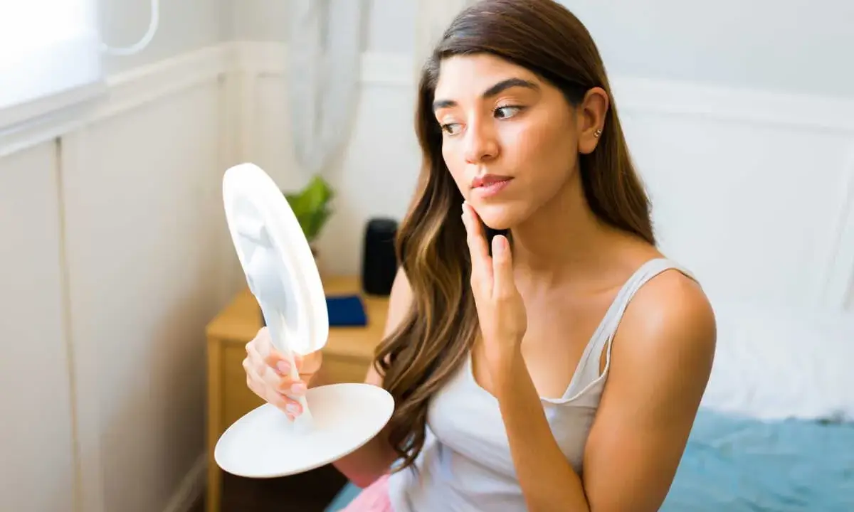 Femme examinant son visage dans un miroir lumineux, cherchant des conseils sur comment maigrir du visage.
