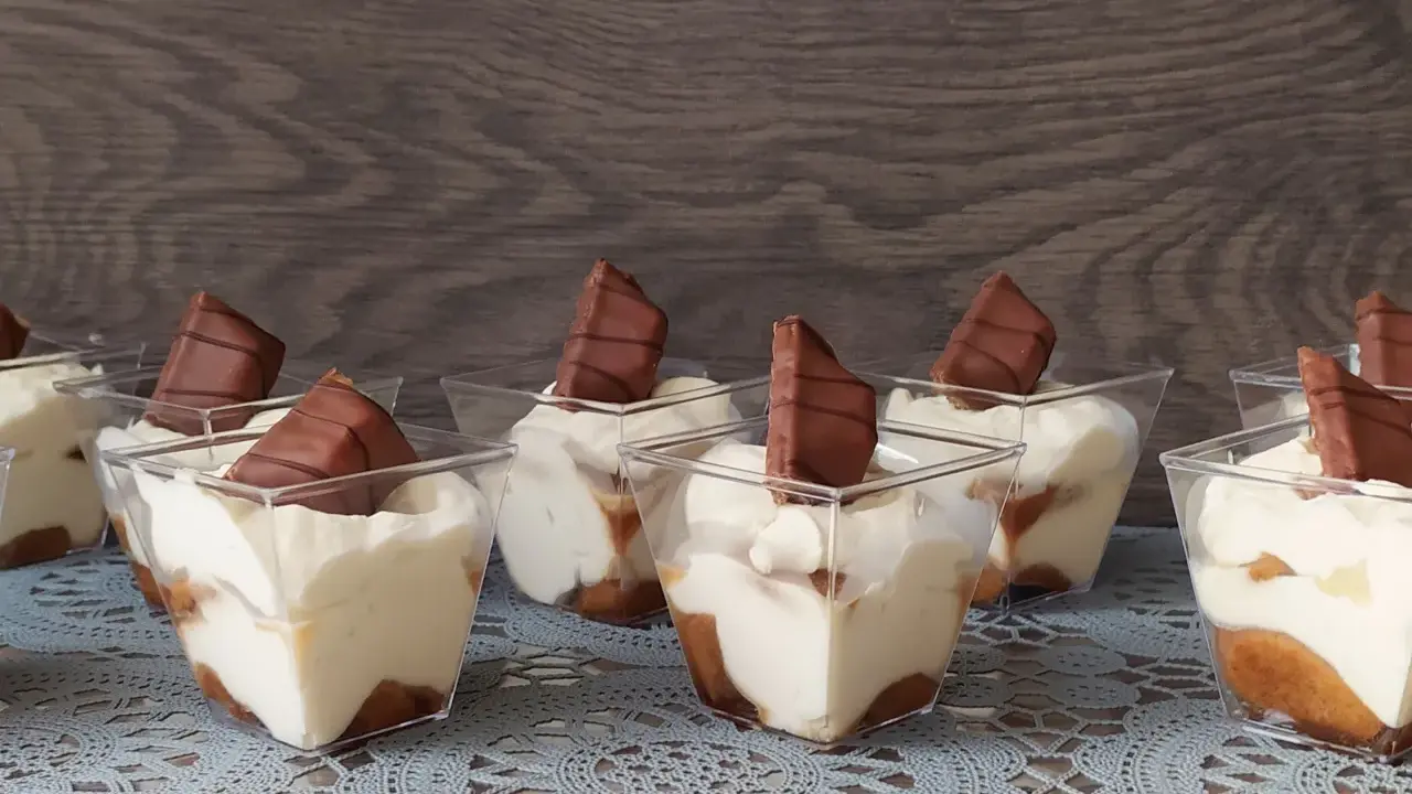 Słodkie deserki w pucharkach, przypominające tort Kinder Bueno, z kremem i kawałkami czekolady.