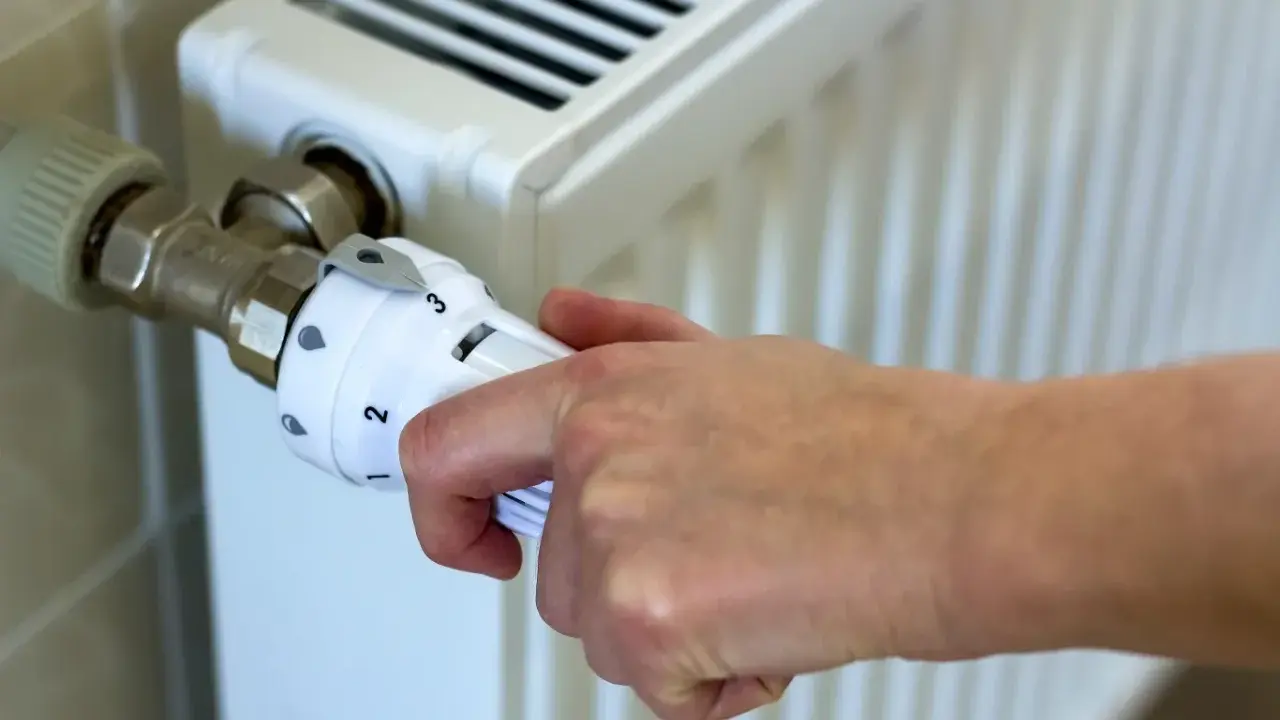 Dłoń reguluje termostat grzejnika. Kiedy zaczyna się sezon grzewczy? Zazwyczaj od października do kwietnia.