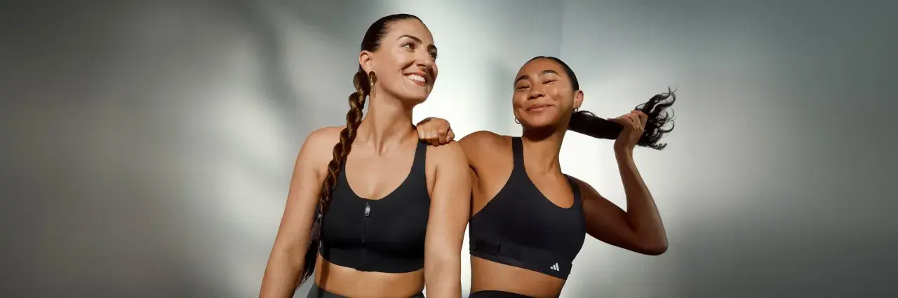 Two women in black sports bras, one with a braid, the other playing with her hair.