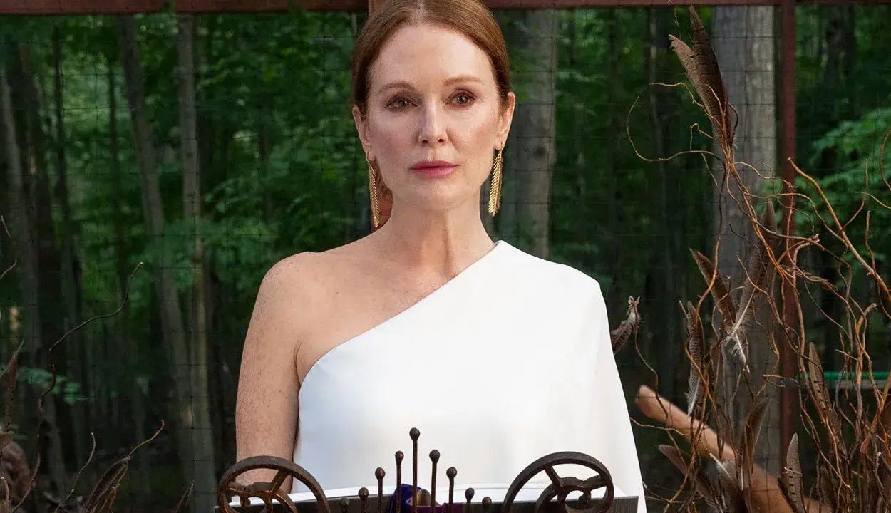 Julianne Moore i den vita klänningen i "Sirens"-serien, med en bakgrund av skog och dekorationer av fjädrar och kvistar.