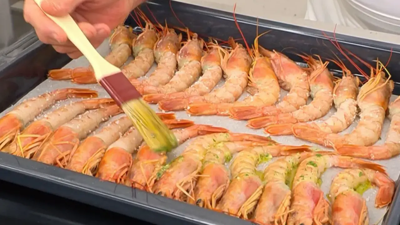 Un pincel baña con aceite y hierbas unos gambones al horno listos para cocinar.