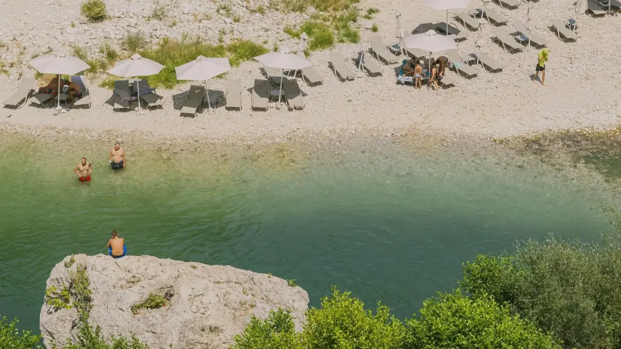 Wczasy w Albanii: ludzie odpoczywają na plaży nad krystalicznie czystą wodą, niektórzy kąpią się, inni relaksują pod parasolami.
