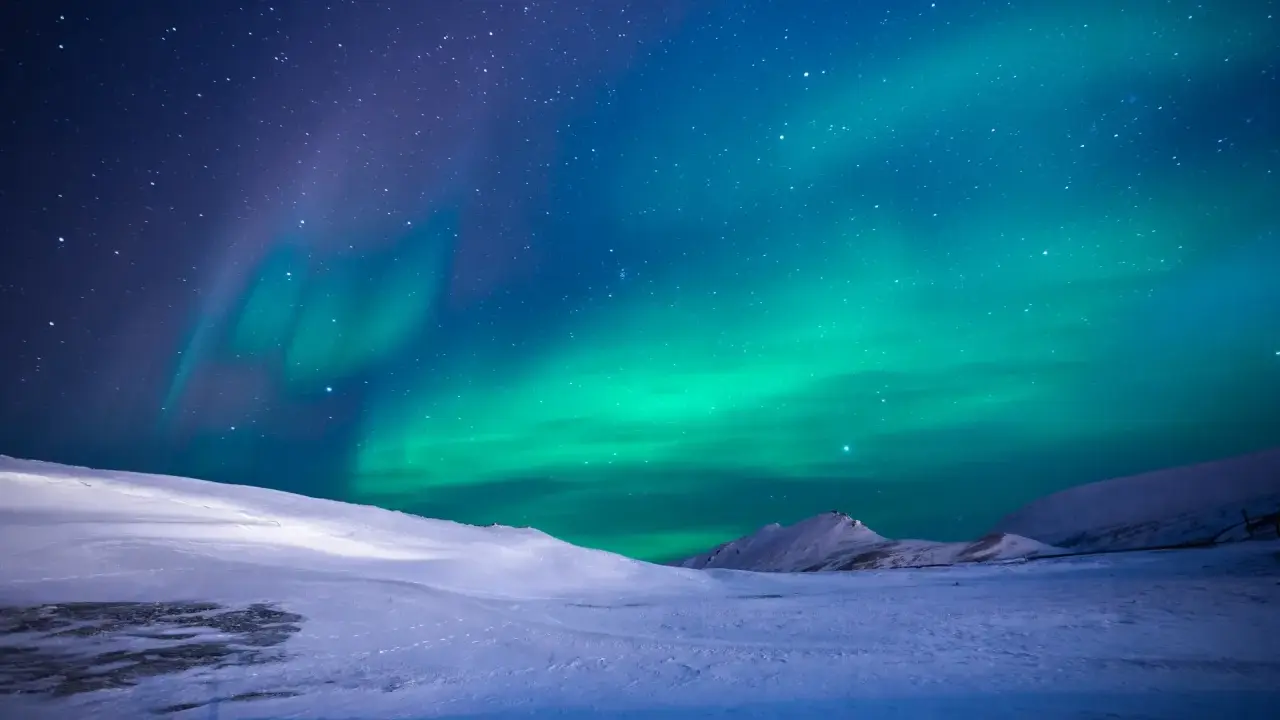 Ett magiskt blått norrsken dansar över en snötäckt fjällvärld under en stjärnklar natt.