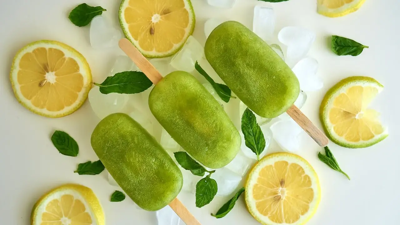 Trois bâtonnets glacés verts, comme une coupe colonel rafraîchissante, entourés de citrons, de menthe et de glaçons.