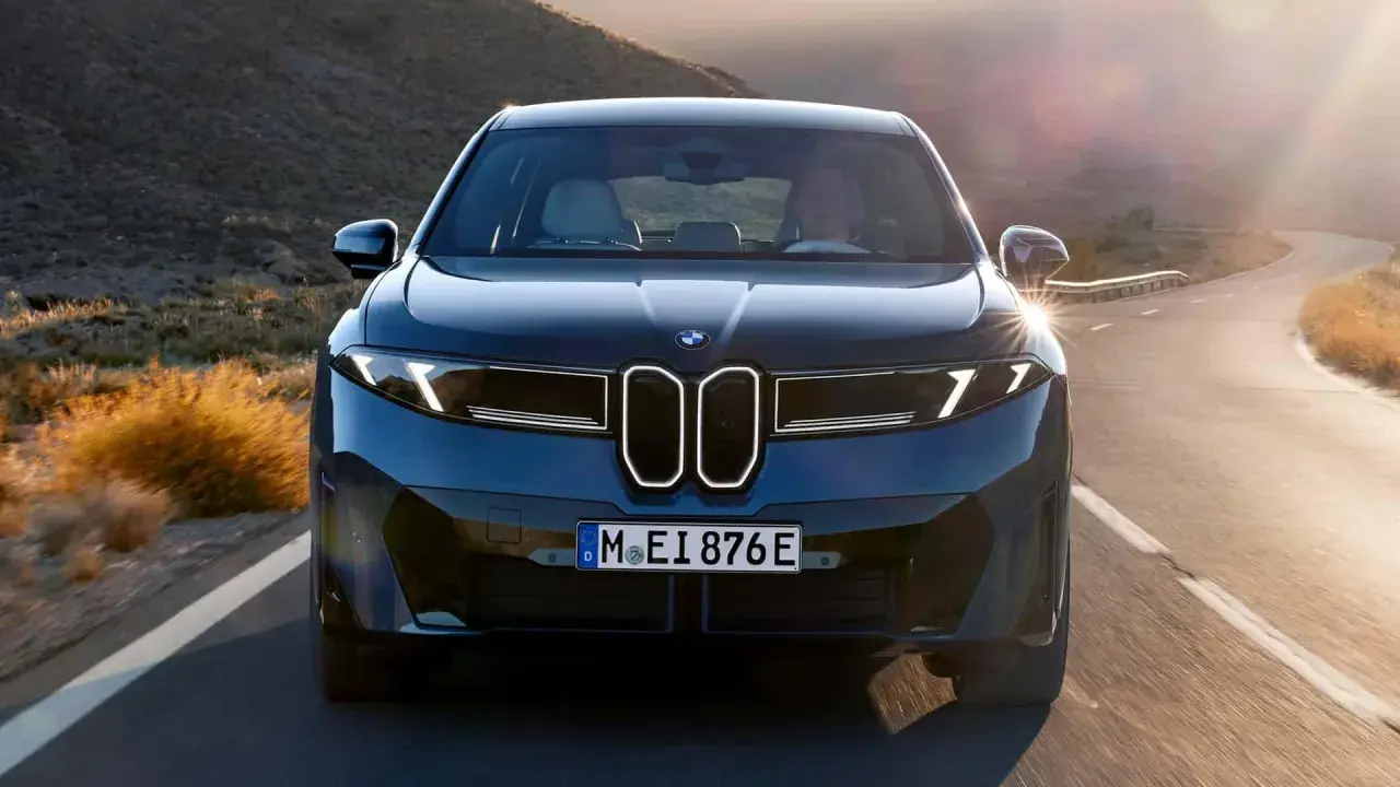 Der BMW iX4 fährt auf einer kurvigen Straße durch eine bergige Landschaft im goldenen Licht der Abendsonne.