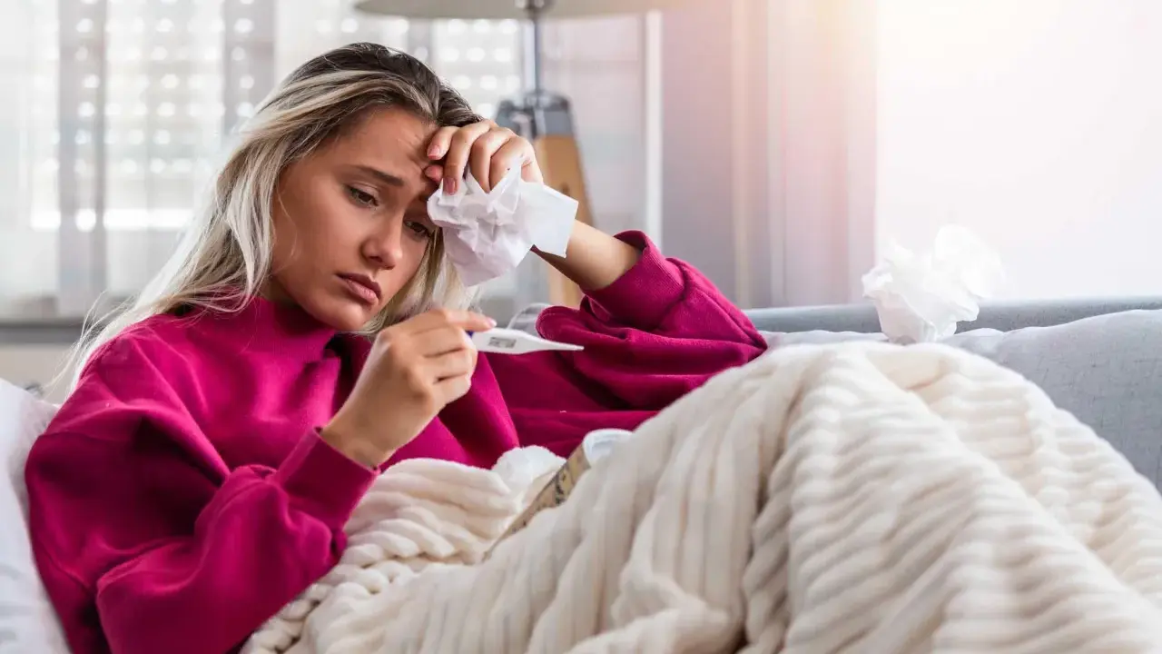 Donna malata con termometro e fazzoletto, preoccupata per il suo stato, forse **immunodepresso significato** da approfondire.