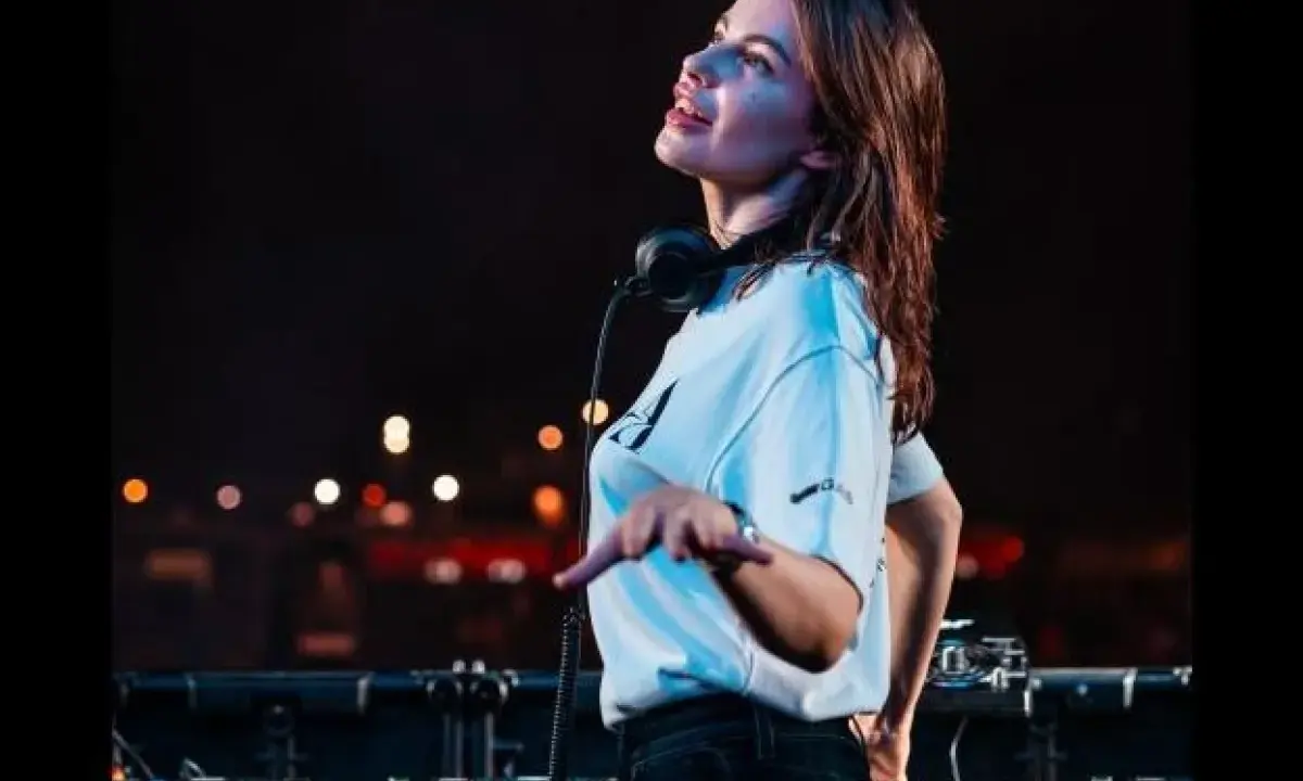 Anfisa Letyago, giovane DJ, con cuffie al collo, mixa musica dal vivo. La sua età è un mistero, ma la sua passione è evidente.