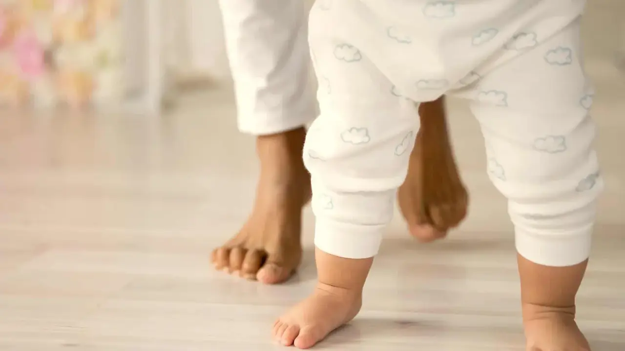 Un bebé da sus primeros pasos, guiado por un adulto. Un momento tierno que ilustra cómo educar a un bebé: con amor y apoyo.