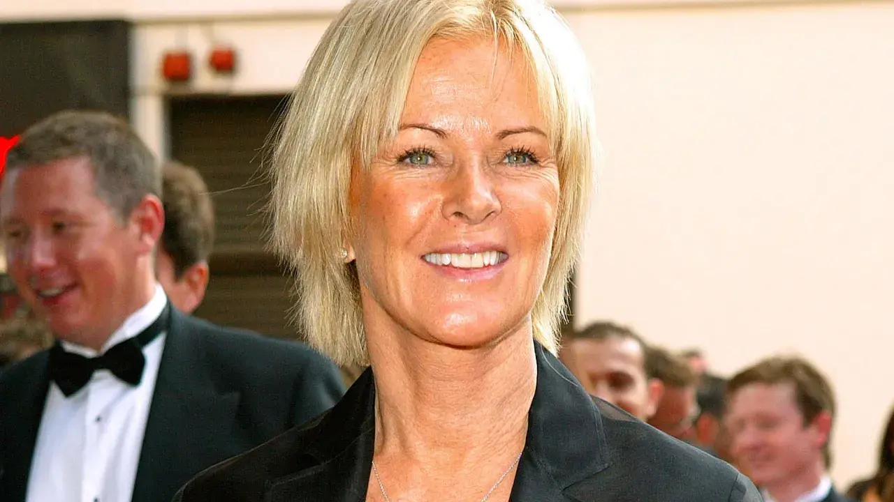 Anni-Frid Lyngstad, känd som Frida, ler med en hjärtformad halsband. Hon är klädd i en svart kavaj.
