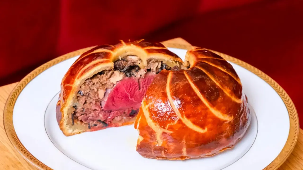 Un pâté en croûte aux couches généreuses, un délice d'antan origine, sur une assiette blanche bordée d'or.