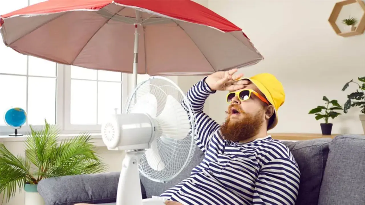 Un homme transpire sous un parasol, ventilateur et plante pour comment rafraichir sa maison. Il a chaud.