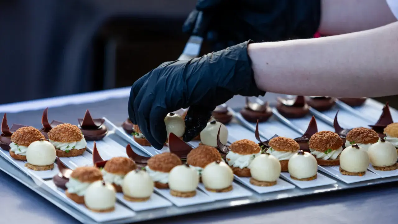 Mains de chef en gants noirs disposant des bouchées, une spécialité culinaire de Metz, sur un plateau.