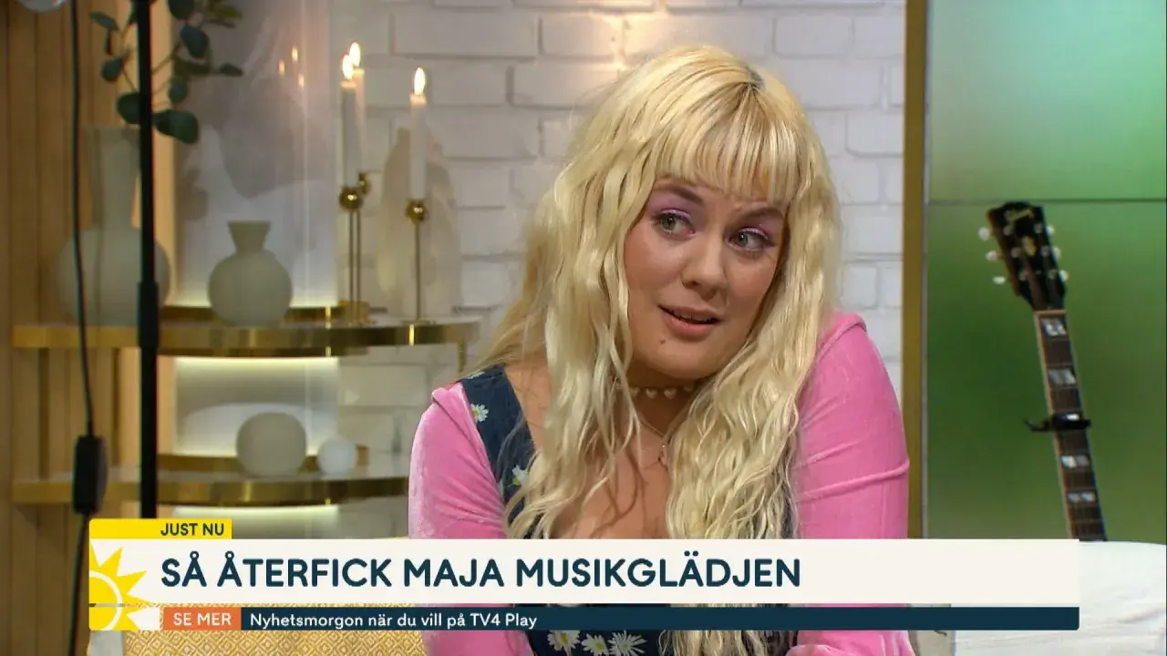 Maja Francis, med sitt blonda hår och rosa tröja, pratar om hur hon återfick sin musikglädje. En gitarr syns i bakgrunden.